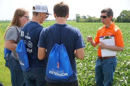 A university professor conversing with students while standing in a soybean field.