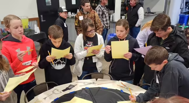 Kids standing around a table, each reading a piece of paper